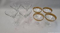 Photo showing set of 8 glasses - 4 clear stemmed cocktail glasses and 4 gold rimmed glasses.