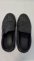 Top front view of black woven leather Bottega Veneta slip-on shoes showing paired shoes side by side.