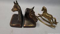 Photo showing two bronze horse head bookends side by side with brass rocking horse placed next to them.