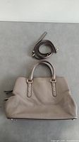 Gray Kate Spade purse shown flat with detachable shoulder strap coiled beside it.