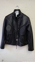 Front view of black leather jacket showing high collar, braided leather detail across chest, and zippered pockets.