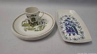 Photo showing all items in the set: one rectangular plate, four round plates, and one cup with folk art design.