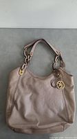 Full view of the light beige Michael Kors purse with double handles and logo charm