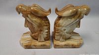 Front view of both carved Onyx marble bookends showing their stylized animal head shape and natural stone patterns.