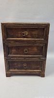 Front view of the small wooden dresser showing three drawers with round metal ring handles and carved frame detailing around each drawer.