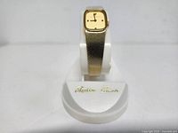 Watch front displayed upright on stand showing gold-tone case and mesh band