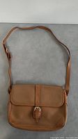 Full front view of tan leather shoulder bag with flap and buckle closure