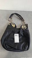 Front view of black leather Michael Kors purse with handles and MK logo charms