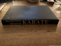 Spine of a hardcover book titled Advanced Karate by Masutatsu Oyama resting on a wooden surface.