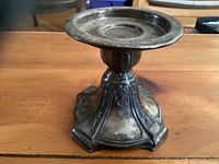 Front and side view of the antique metal candle holder showing detailed ornate patterns and dark tarnished patina.