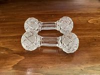 Pair of antique clear glass utensil rests with intricate cut patterns on a wooden surface.