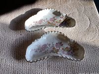Pair of curved white porcelain bone dishes with pink and orange floral designs, viewed from top under natural light