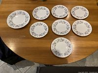 Top view of all eight plates arranged on a wooden table showing a set of seven smaller and one larger plate with floral pattern.