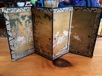 Four-panel Japanese folding screen standing upright on a wooden surface, decorated with cranes and bamboo artwork on a gold background.
