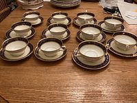 Full display of 6 teacups with saucers and cream soup bowls arranged on a wooden table, showing the matching cobalt blue and gold pattern.