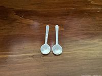Two small mother of pearl spoons side by side on wooden surface, viewed from the bowl side