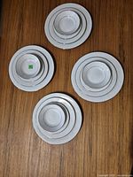 Top down view of all 16 dishes grouped in sets of four, showing four sizes of plates and bowls with white base and silver floral border.