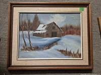 Front view of framed oil painting showing a winter barn scene covered in snow with leafless trees.