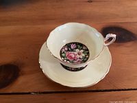 Porcelain cup and saucer set showing floral pattern and gold trim. Cup with X-shaped crack visible.
