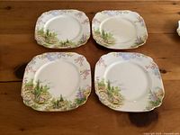 Four square plates with floral and rockery scenic design and gold trim on wooden table