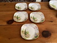 Top-down photo showing 5 square bread plates with scenic floral countryside pattern in soft colors.