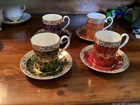 Photo of the four espresso cups with handles visible, colors blue, coral, green, and red, decorated with gold floral patterns.