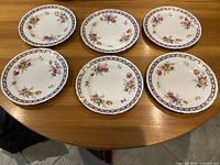 Top view of six Royal Crown Derby lunch plates arranged on a wooden table, showing the full floral Spring pattern and blue border on each plate.