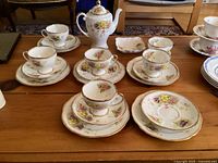 Full view of the Royal Standard Charmaine tea set items arranged on a wooden table, showing cups, saucers, plates, cocoa pot, sugar bowl, and square dish, in excellent condition.