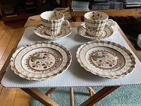 Set of 2 cups and saucers and 2 bread plates arranged on a table showing floral Cowslip pattern with scalloped edges.