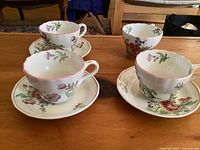 Four ceramic tea cups and three matching saucers with floral patterns and pink rims on a wooden table.