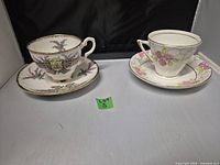 Two English teacup and saucer sets on display, showing floral and patterned designs with gold trim