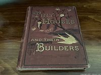 Front cover of antique book 'Tiny Houses and Their Builders' showing embossed gold lettering and illustration on a brown cloth cover.