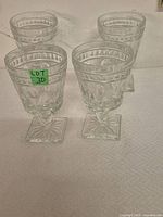 Four clear vintage pressed glass goblets standing upright on a textured white cloth background.