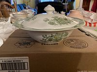 Side view of round vegetable bowl with covered lid, showing floral pattern and green border.
