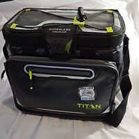 Front view of the black Arctic Zone Titan zipperless can cooler showing zippered pocket and front flap.