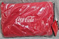 Red Coca Cola sports fleece blanket sealed in clear plastic packaging showing the Coca-Cola embroidered logo.