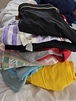 Pile of assorted vintage folded clothing in various colors and patterns including black, white, yellow, red, light blue, and multicolor.