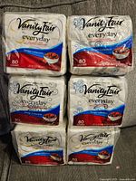 Six packs of Vanity Fair Everyday printed napkins in original packaging. Each pack contains 80 napkins, featuring a stylish swirl design on the packaging with red and blue accents.