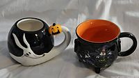 Pair of Disney-themed Halloween mugs on a white cloth background, one shaped like Zero the ghost dog with a pumpkin on the handle, the other shaped like a witch's cauldron with Minnie Mouse witch design.