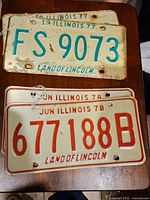 Front view of 1977 Illinois license plates with turquoise text showing wash wear and rust.