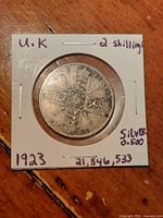 Obverse side of the 1923 United Kingdom one florin coin in protective cardboard holder with handwritten notes about the coin denomination, year, and silver content