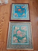 Top view of two framed antique Chinese embroidered silk panels laid on a wooden floor showing detailed embroidery and frames.