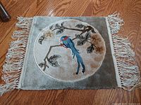 Top down photo of the woven silk tapestry laid flat, showing the full square with tassels and the bird design inside a circular frame.
