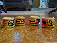 Four handcrafted wooden napkin rings with painted First Nations designs placed on a wooden floor for size and detail view.