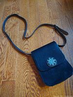 Full leather bag with long adjustable strap laid flat on wooden floor showing front and shape