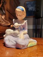 Front view of vintage Royal Doulton figurine showing girl in lavender dress with lamb on lap.