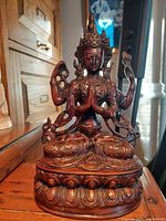 Front view of the Vasudhara statue showing detailed facial features, crown, hands in prayer and holding symbols, along with ornate base.