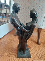 Front right angle view showing the male and female figures in close embrace on wooden floor next to chair leg.