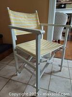 Front and side view of vintage directors chair with white wood frame and yellow/white striped textile seat and back.