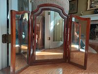 Front view of a vintage three pane articulated makeup mirror with wooden frames, showing all three panels with the side panels slightly angled inward revealing the hinge mechanism.